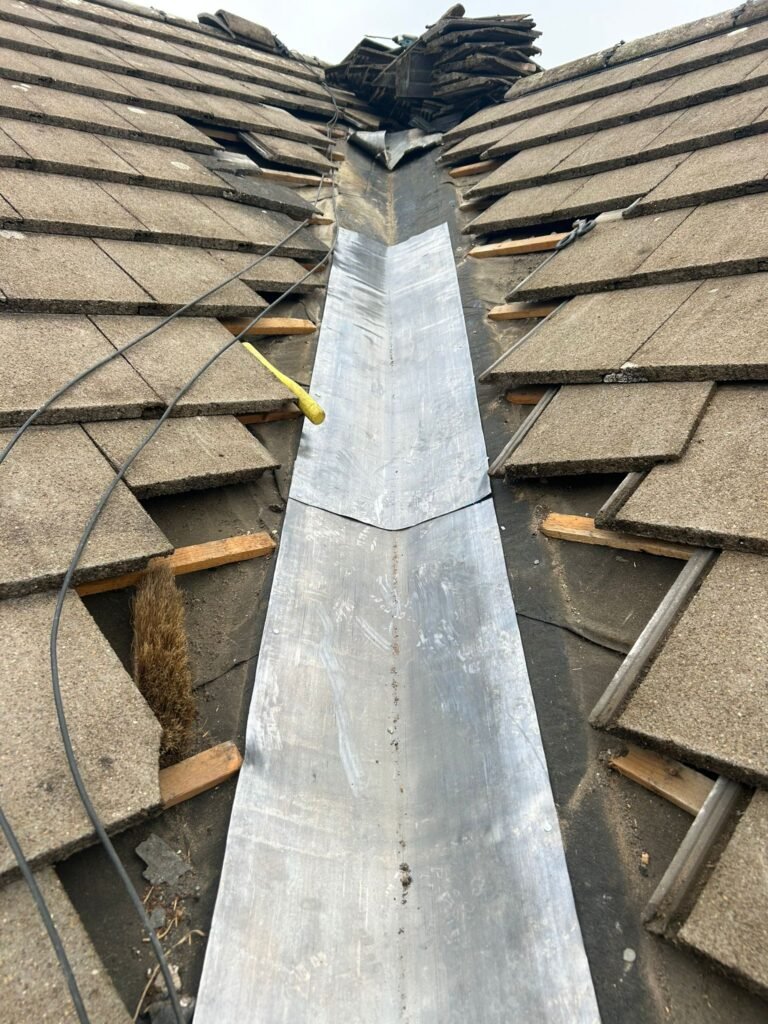 Lead valley roof flashing installation in progress with concrete roof tiles removed for roofing repair and waterproofing work.